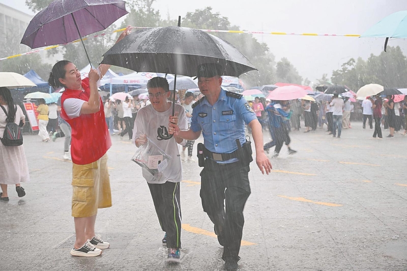 6月14日，在六安市金寨一中考点，志愿者与民警一起在雨中为考生撑伞。.jpg